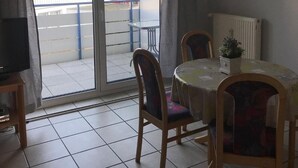 Et værelse med spisebord, stole, fjernsyn og en skydedør, der fører ud til en balkon.