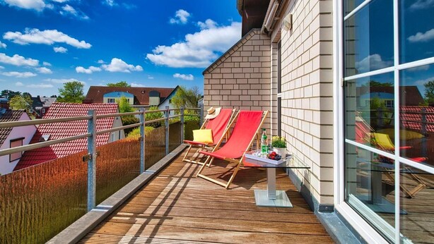 A balcony with a wooden deck, two red lounge chairs, and a glass door leading to a room.