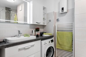 Ein modernes Badezimmer mit Waschbecken, Spiegel, Dusche und einer integrierten Waschmaschine.