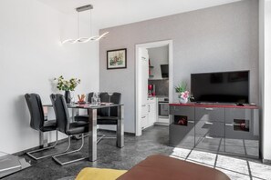 Une cuisine moderne équipée d’un téléviseur à écran plat, d’un coin repas avec des chaises et une table, et d’un petit espace de vie avec un canapé.