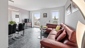 A modern living room with a red leather sofa, a glass coffee table, and a dining area with a black chair and a table.