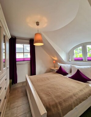 Ein Schlafzimmer mit Bett, Nachttisch, Lampe, einem Fenster mit Vorhängen und einer Deckenleuchte.