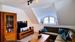 A loft-style living room with a high ceiling, a wooden cabinet, a flat-screen TV, a sofa, and a coffee table.