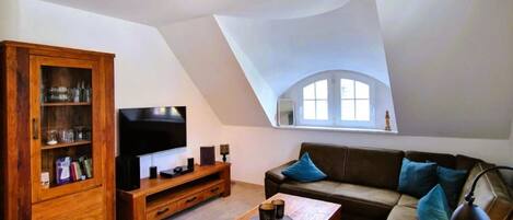 A loft-style living room with a high ceiling, a wooden cabinet, a flat-screen TV, a sofa, and a coffee table.