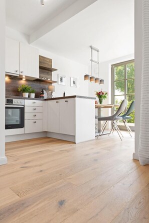 Eine moderne Küche mit weißen Schränken, einem eingebauten Backofen und einem Essbereich mit Tisch und Stühlen.