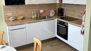 Een compacte keuken met witte kastjes, een houten aanrecht, een spoelbak, een koffiezetapparaat en een fornuis.