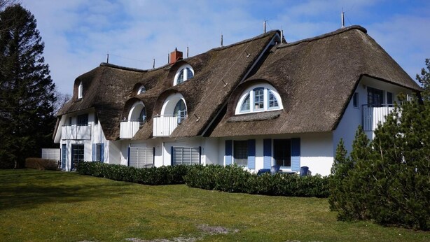Een traditioneel rieten huis met meerdere ramen en een verzorgd gazon.