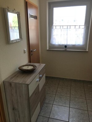 A bathroom with a wooden vanity, a sink, a mirror, a door, and a window with a view of a fence.