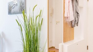 Quarto com um espelho grande, um vaso de planta, um cabideiro com roupas e uma mala grande.
