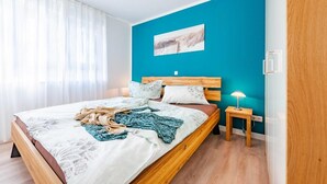 Quarto com cama de madeira, roupa de cama branca, parede azul e luminária de cabeceira.