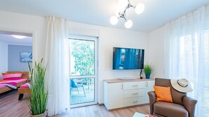 Uma sala de estar moderna com sofá, televisão, mesa de jantar com maçãs e varanda com vista para árvores.