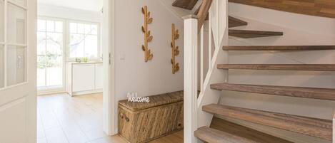 Una escalera con escalones de madera y barandilla blanca, que lleva a una habitación con puerta y ventana blancos.