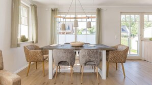 A dining area with a wooden table, cushioned chairs, and a hanging light fixture. - Haseneck 2a " Kranichfeld" - central and yet quietly situated vacation home for (Zingst)