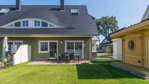 A two-story house with a dark tiled roof, a covered patio with a table and chairs, and a well-maintained lawn. - Haseneck 2a " Kranichfeld" - central and yet quietly situated vacation home for (Zingst)