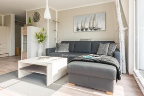 Ein modernes Wohnzimmer mit einem grauen Sofa, einem weißen Couchtisch und einem Bild von Segelbooten an der Wand.