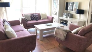 Een woonkamer met een roze zithoek, een witte salontafel en een televisie op een witte dressoir.