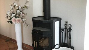 Een zwarte houtkachel met glazen deur, een witte vaas met bloemen en een witte mand met hout.