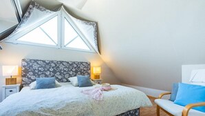 Een slaapkamer met een bed, twee nachtkastjes, een stoel en een raam met gordijnen.