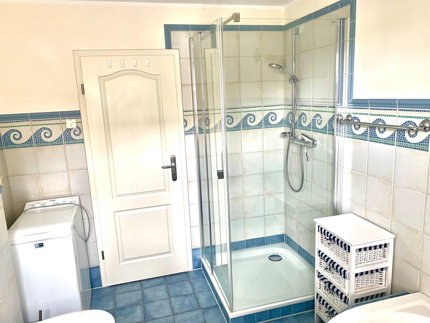 A bathroom with a glass shower enclosure, a white door, and a tiled floor.