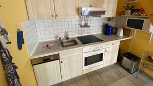 Una cocina compacta con armarios blancos, un lavamanos de acero inoxidable y un horno empotrado.