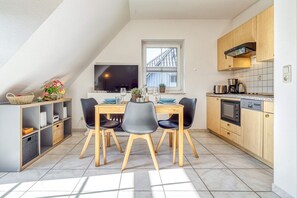 Uma cozinha moderna com área de refeições, apresentando uma televisão, armários de madeira e piso revestido de azulejos.