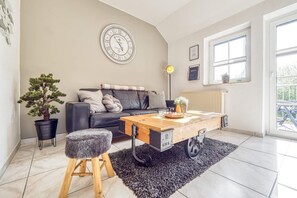 Uma sala de estar aconchegante com um sofá de couro preto, uma mesa de centro de madeira, uma planta em vaso e um relógio de parede grande.