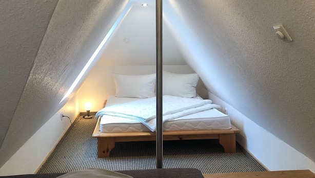 A small, triangular attic bedroom with a bed, a nightstand, and a bench.