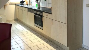 A modern kitchen with light wood cabinets, a stainless steel oven, and a window providing natural light.