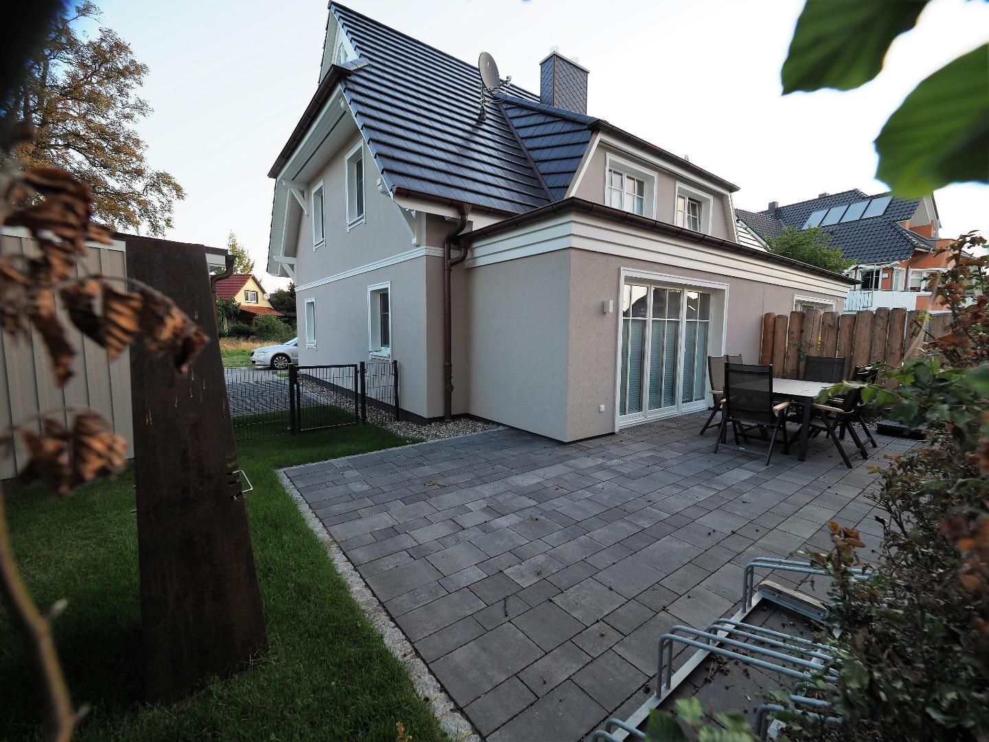 A two-story house with a tiled patio, a wooden fence, and a car parked in the driveway.