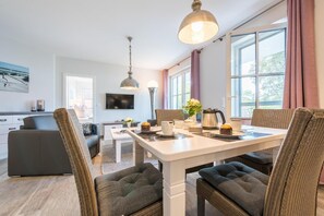 Ein modernes Wohnzimmer mit Essbereich, ausgestattet mit einer Couch, einem Couchtisch und einem Esstisch, gedeckt mit Tassen und einem Wasserkocher.