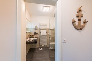 Een moderne badkamer met een douchecabine van glas, een witte wastafel met spiegel en een houten ankerdecoratie aan de muur.