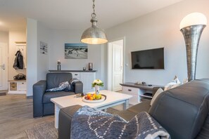 Ein modernes Wohnzimmer mit einer Couch, einem Couchtisch mit Früchten, einem Fernseher und einer einzigartigen Stehlampe.