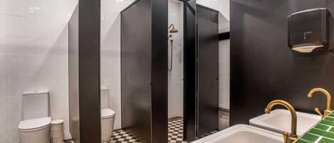 Een badkamer met een zwart-wit betegelde vloer, twee wastafels met gouden kraanwerk, een douche en een toilet.