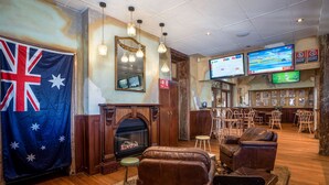 Un área de estar con chimenea, sofás de cuero, suelo de madera y una zona de bar con varias pantallas.