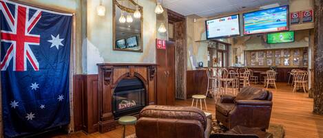 A lounge area with a fireplace, leather sofas, wooden flooring, and a bar area with multiple screens.