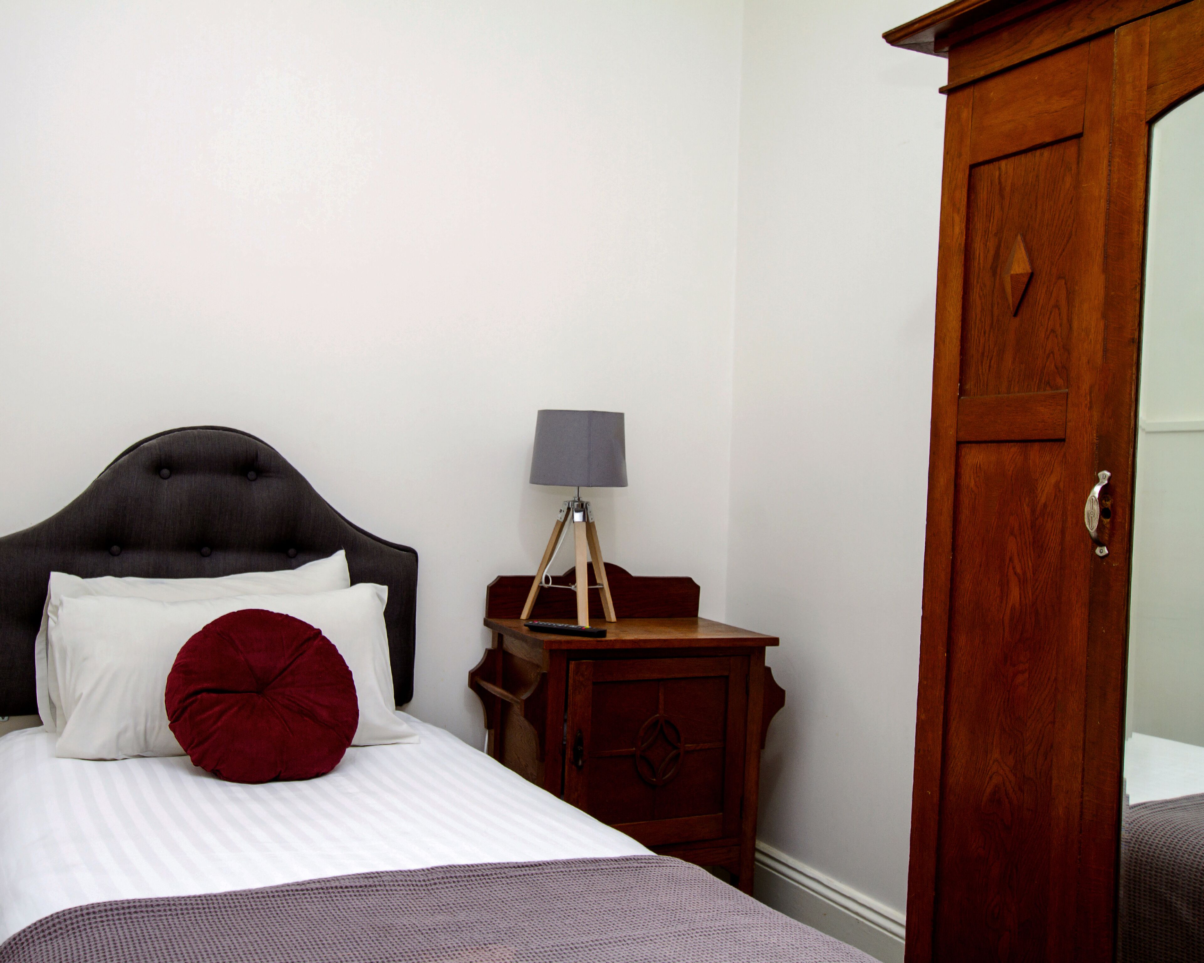 A neatly made bed with white and red pillows, a bedside lamp, and a wooden nightstand.