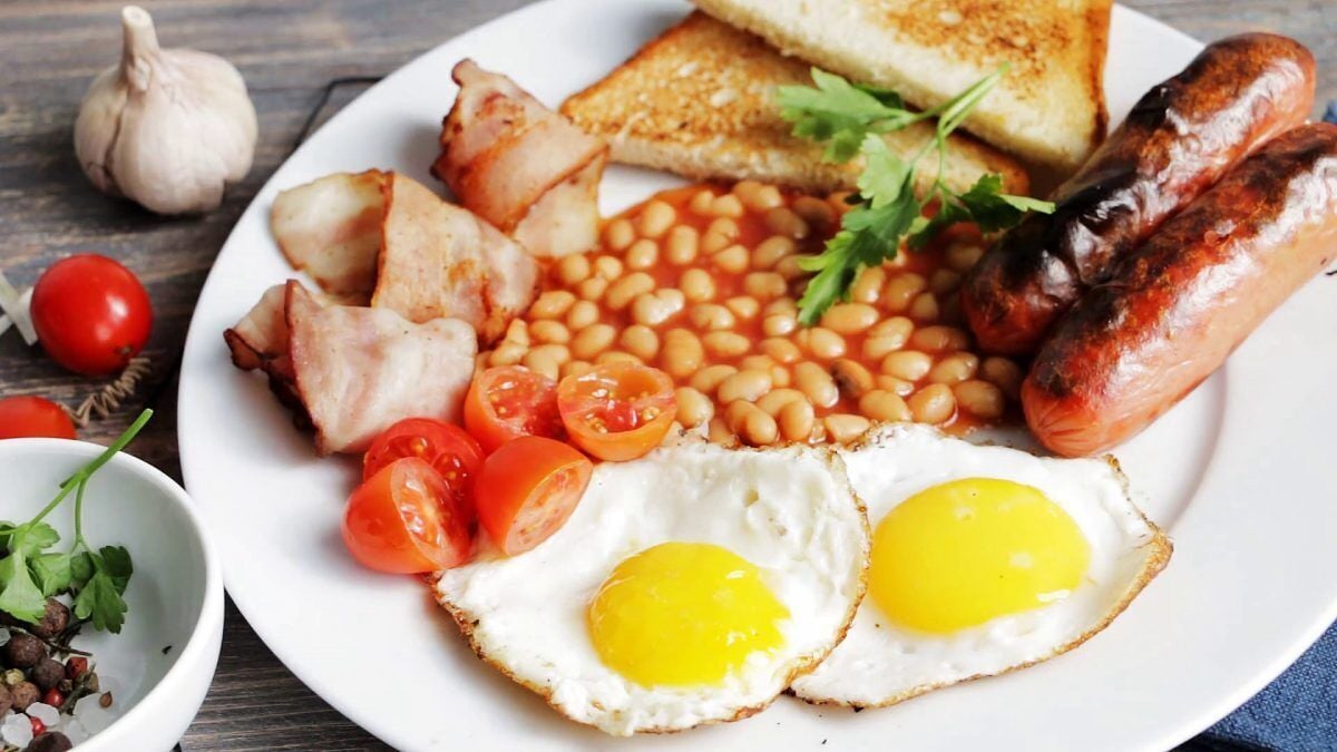 A plate of breakfast food including eggs, sausages, beans, toast, and tomatoes.