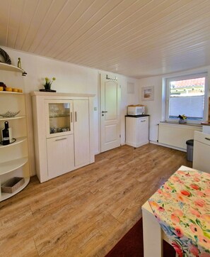 A compact kitchen with wooden flooring, white cabinetry, and a window with blinds.