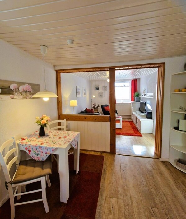 A cozy room with a dining table, chairs, a red rug, and a view into another room with a red curtain.