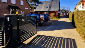 Una calle residencial con casas, un acceso con reja y automóviles estacionados.