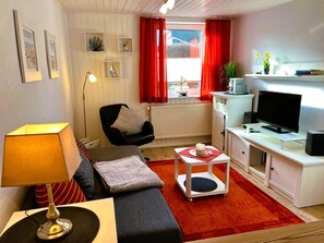 A compact living space with a sofa, a desk with a computer, a TV, and a small table with a cake.