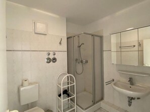 Uma casa de banho moderna com chuveiro em cabine de vidro, sanita, lavatório e porta-toalhas.