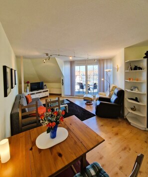 Ein modernes Wohnzimmer mit einem Holzespeisetisch, einer Couch, einem schwarzen Sessel und einem Bücherregal.