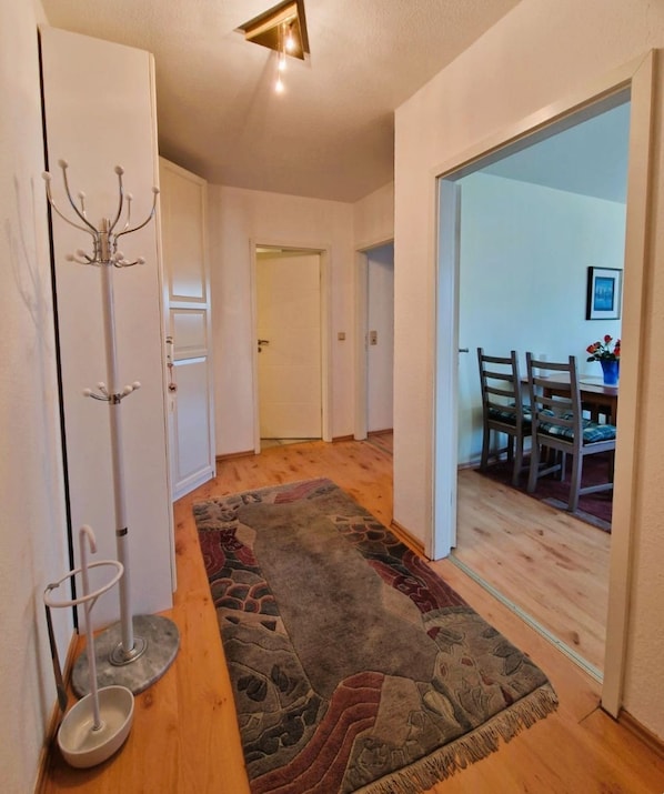 A hallway with a patterned rug, a coat rack, and a dining area visible through an open door.
