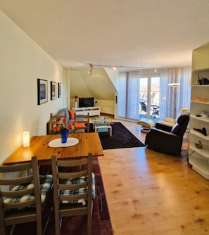 A cozy living room with a wooden dining table, chairs, a sofa, and a TV.