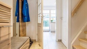 Un corridoio moderno con una panca in legno, un appendiabiti con giacche blu e vista su un balcone con una pianta.