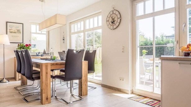 Un'area pranzo moderna con tavolo in legno, sedie nere e una grande finestra.