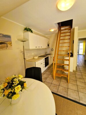 Una cucina con mobili bianchi, una scala di legno, un tavolo da pranzo con un vaso di fiori e un pavimento piastrellato.