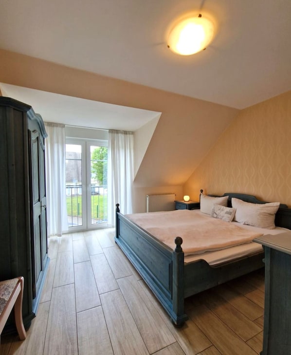 A bedroom with a large bed, a nightstand, a dresser, and a view of the outside.