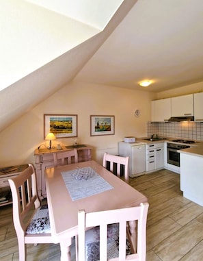 A cozy kitchen with a dining area, featuring a table with chairs, a lamp, and two framed pictures on the wall.